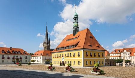 Farbige Gebäude mit roten Dächern und Türmen unter blauem Himmel mit Wolken.
