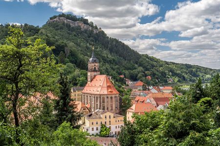 Blick auf eine Stadt mit bunten Häusern und einer Kirche, umgeben von grünen Hügeln und Wolken.