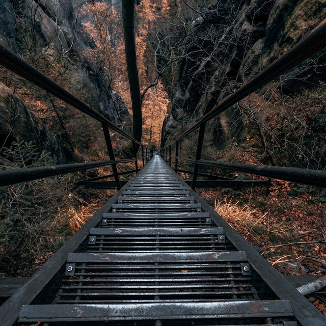 Blick auf eine steile Metalltreppe, die in einen dunklen Raum führt, umgeben von glühenden orangefarbenen Lichtern.