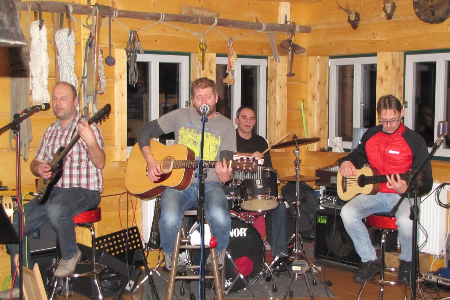 Vier Musiker spielen in einer Holzstube. Zwei mit Gitarren, einer am Schlagzeug und einer singt.