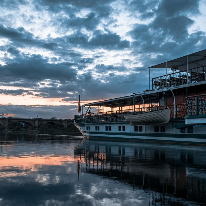 Dampfer am Ufer mit reflektierendem Wasser und dramatischem Abendhimmel.