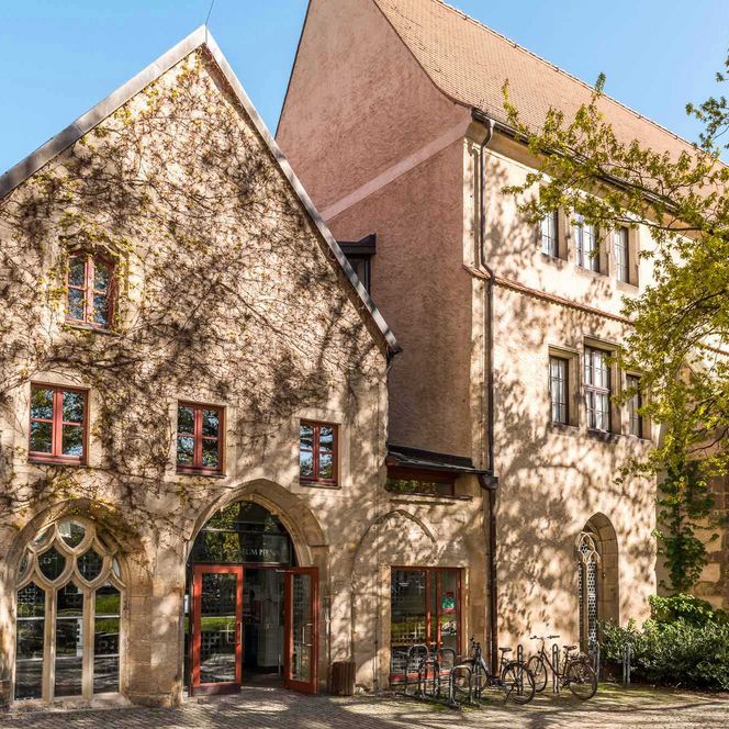 Zwei historische Gebäude mit Steinfassade und grünen Pflanzen im Vordergrund.