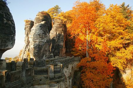 Steinerne Bastei-Brücke neben großen Felsen von bunten Herbstbäumen umgeben. 