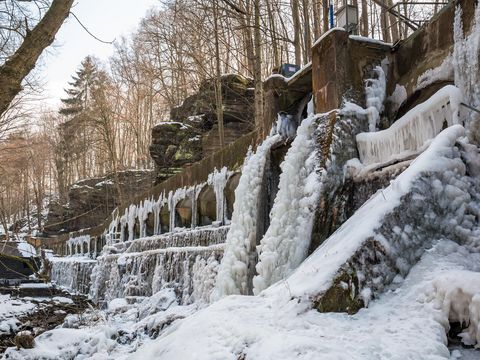 Wesenitzklamm Lohmen mit Felsen und Bäumen, bedeckt mit Schnee, sanftes Sonnenlicht.