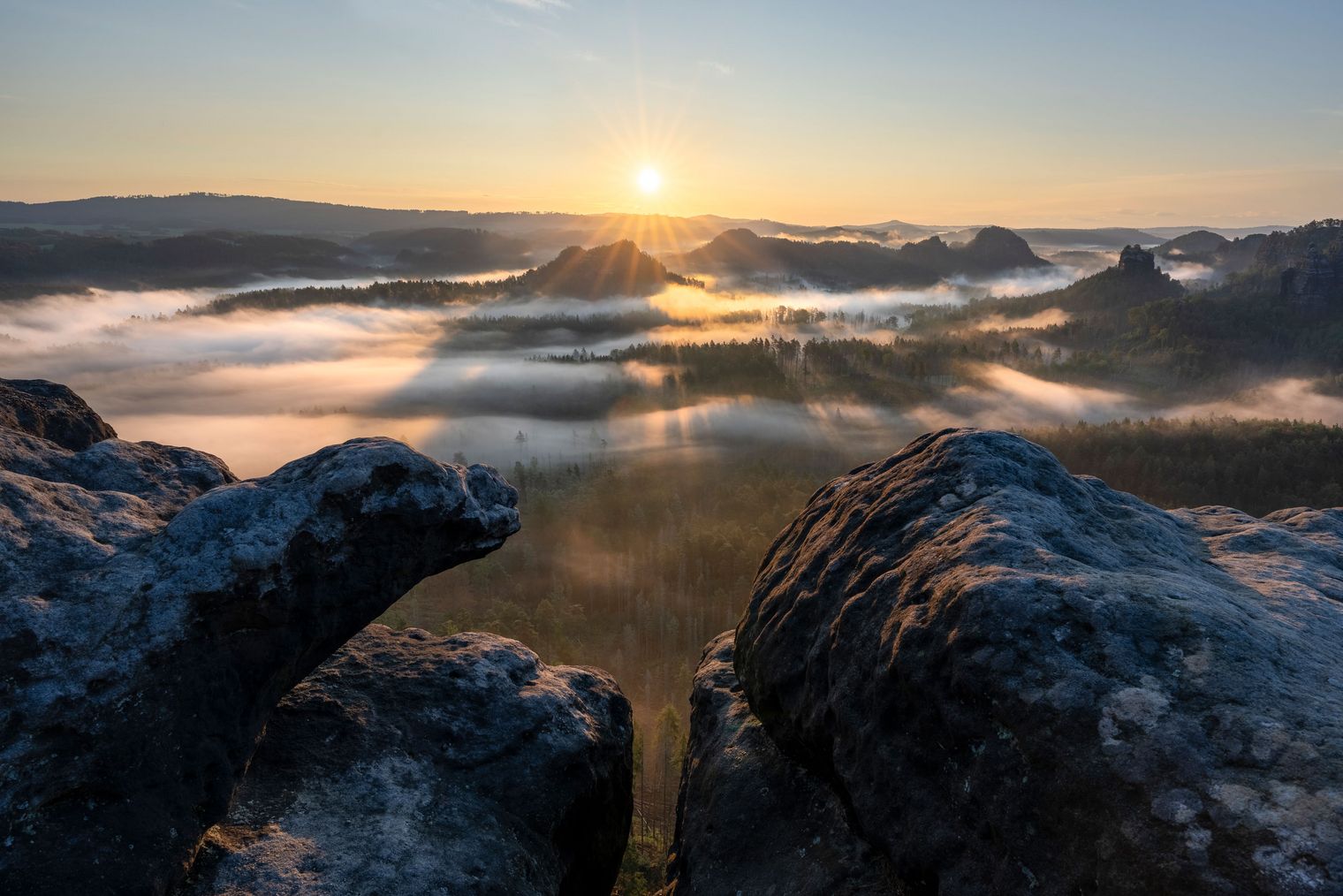 Sonnenaufgang über einer nebligen Berglandschaft, Felsen im Vordergrund.