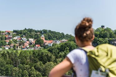 Frau mit Rucksack blickt auf grüne Landschaft und die Dächer der Stadt Hohnstein