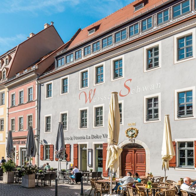 Farbige Gebäude mit Fenstern und Schildern, darunter Tische und Stühle im Freien.