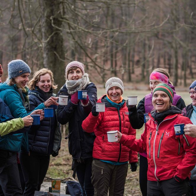 Gruppe von zehn Personen in warmer Kleidung, die Tassen in die Höhe halten, umgeben von Bäumen.