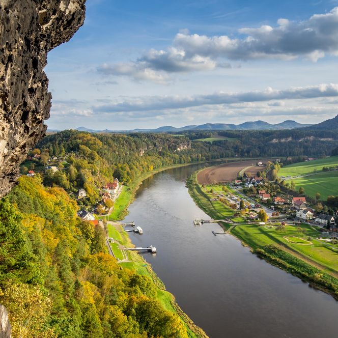 Blick auf einen Fluss, umgeben von grünen Hügeln und bewaldeten Ufern, mit Booten auf dem Wasser.