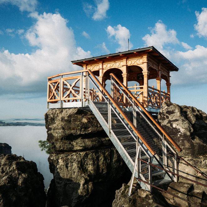 Holzplattform auf einem Felsen mit Treppe, umgeben von einem Nebelmeer.