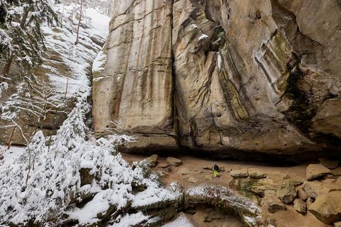 Hohe, schneebedeckte Felsen mit sichtbaren Schichten und einer kleinen Baumgruppe im Vordergrund.