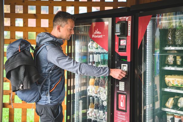 Wanderer steht vor Proviantomat in Rathen, gefüllt mit Snacks und Getränken.