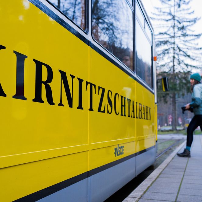 Person läuft an einer gelben Straßenbahn mit der Aufschrift "KIRNITZSCH" vorbei.