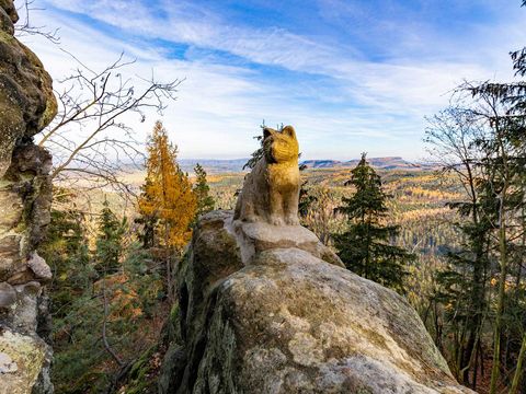 Herbstliche Stein in Form einer Katze in Waldlandschaft mit Felsen und Fernblick auf Hügel unter blauem Himmel.