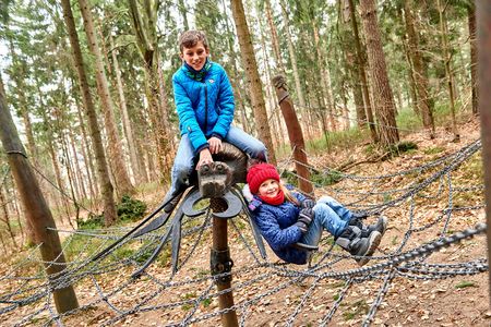 Zwei Kinder spielen auf einem Klettergerüst aus Seilen im Wald.