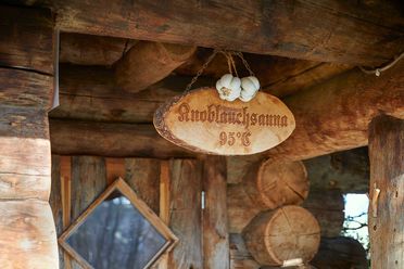 Holzschild mit der Aufschrift "Knoblauchsauna 95 Grad" und zwei Knoblauch-Knollen, umgeben von rustikalen Holzwänden.