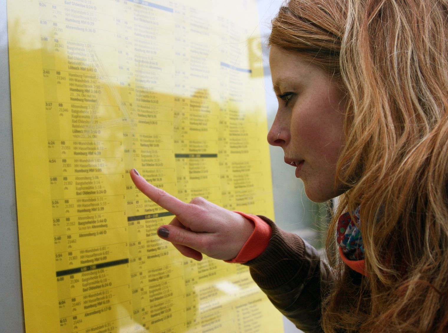 Frau mit langen, roten Haaren zeigt mit dem Finger auf eine gelbe Anzeige mit Informationen.