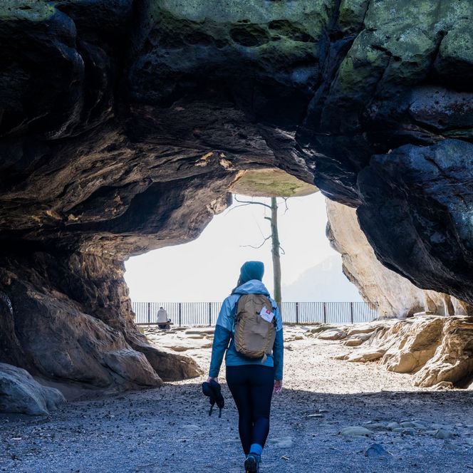 Wanderer mit Rucksack geht durch eine große Felsöffnung ins Freie.