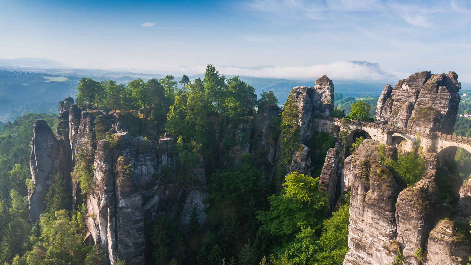Felsformationen der Bastei mit Brücke, umgeben von üppigem Wald unter klarem Himmel.