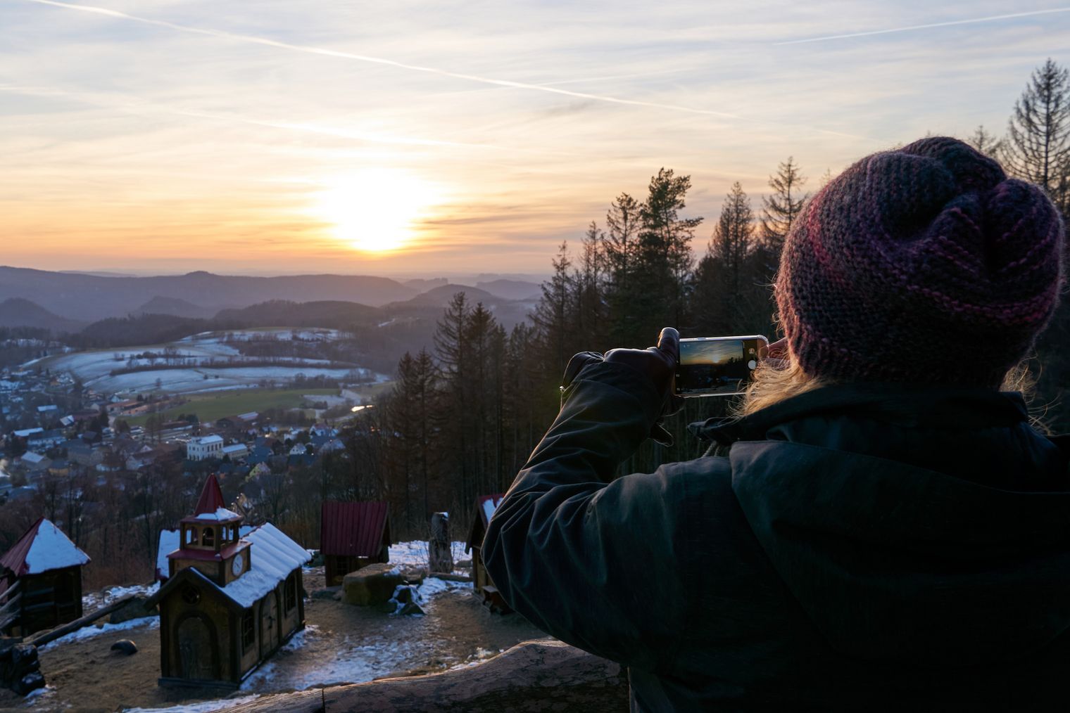 Person mit Kamera beobachtet den Sonnenuntergang am Wachberg über einer winterlichen Landschaft.