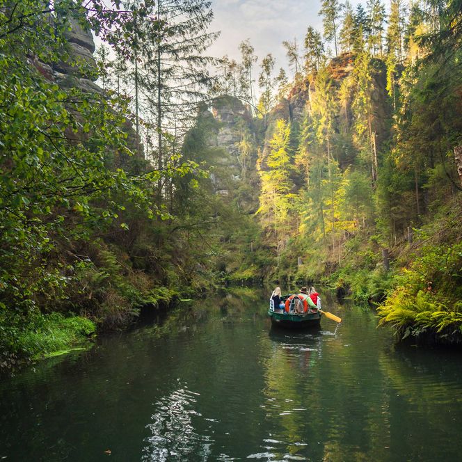 Ruderboot auf einem ruhigen Fluss, umgeben von grünen Bäumen und steilen Felsen.